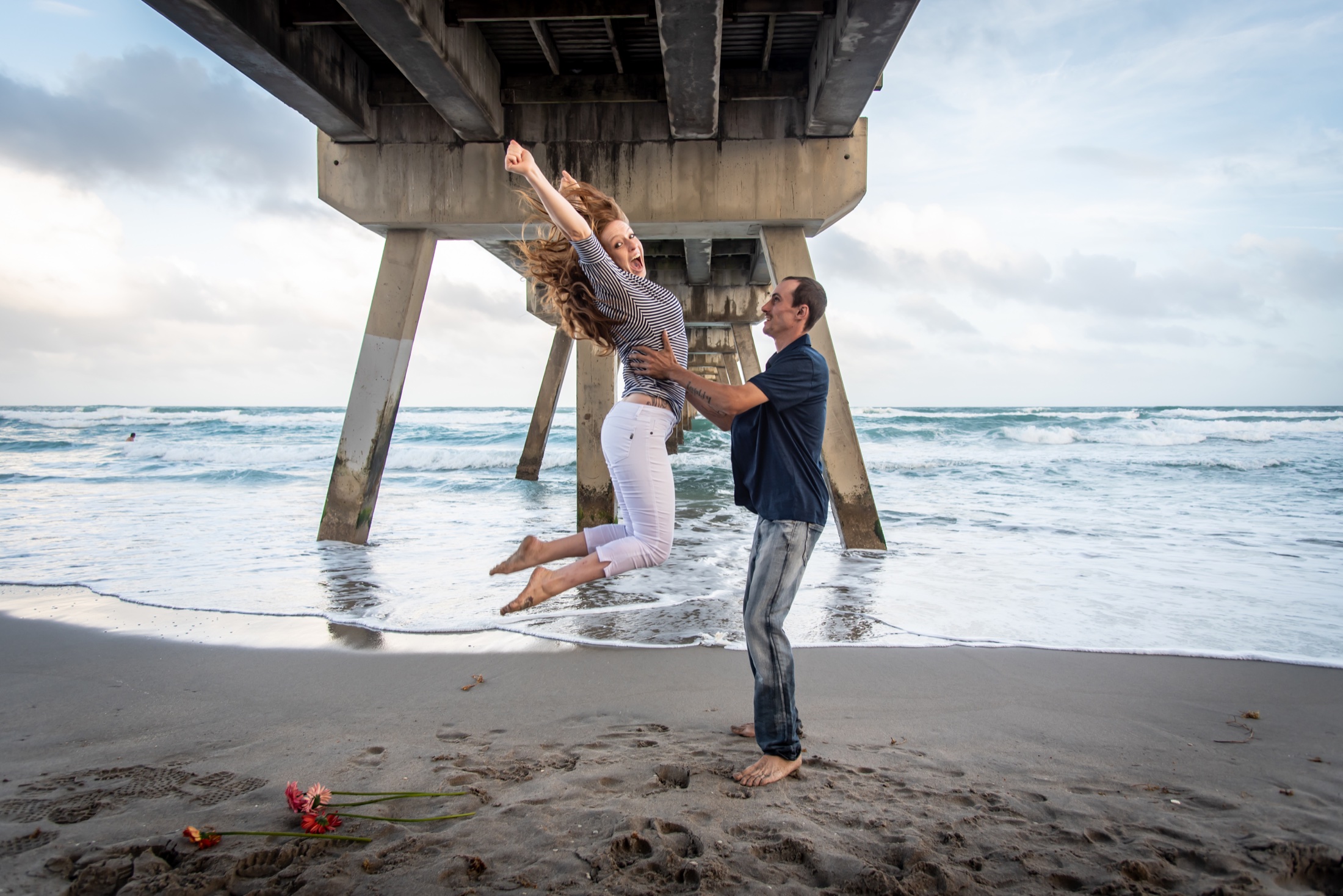 Expectant couple sharing a playful moment beneath a beach pier