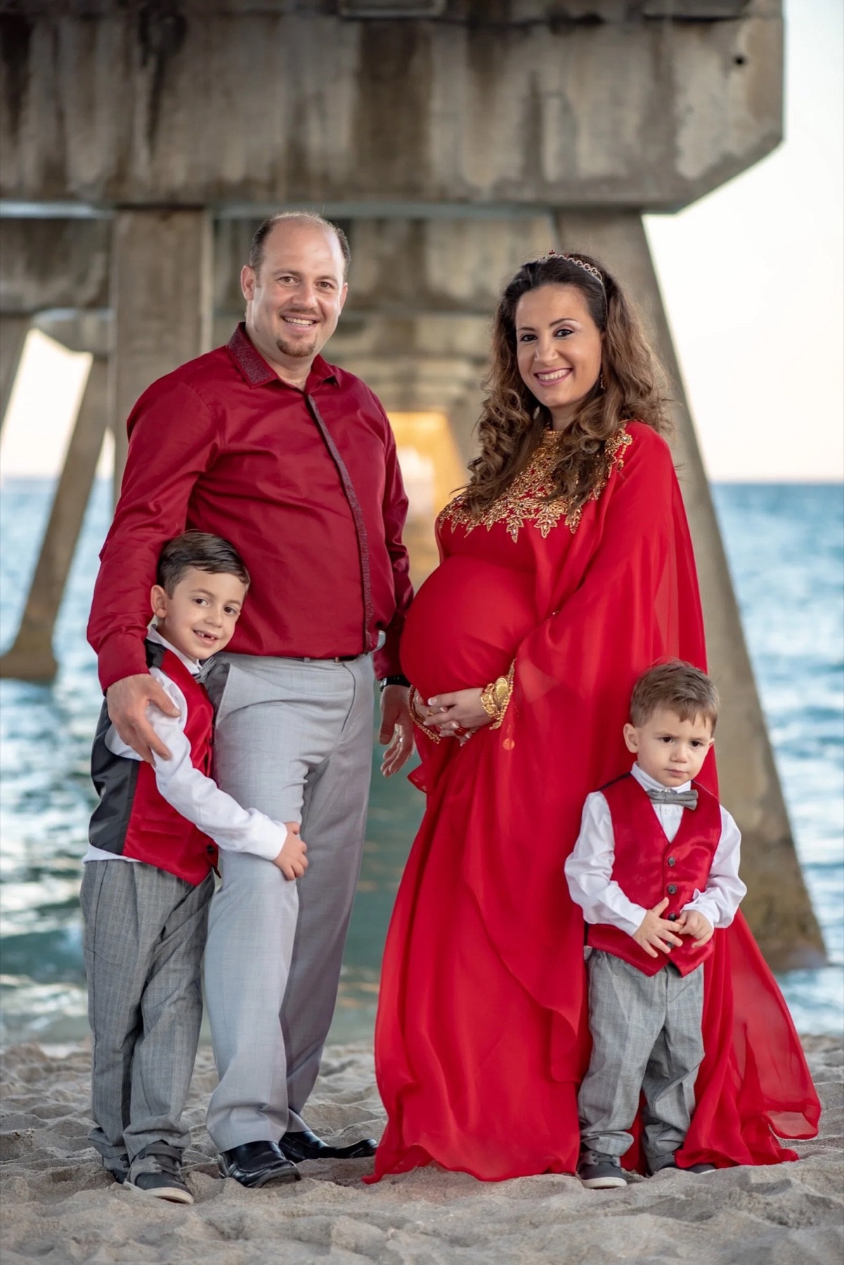 Expectant mother in red photographed with her family on the beach